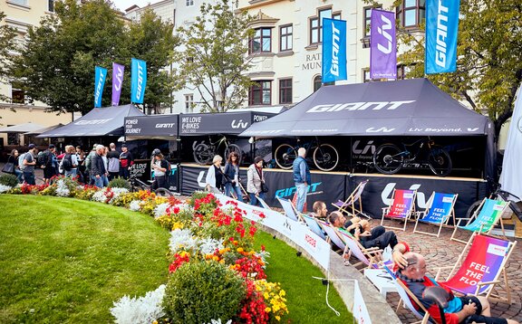 A képen két lapos tetejű, összecsukható pavilon és két csúcsos tetejű, összecsukható pavilon látható. A tetőn zászlók láthatóak. Minden összecsukható pavilonban van pult és személyre szabott.