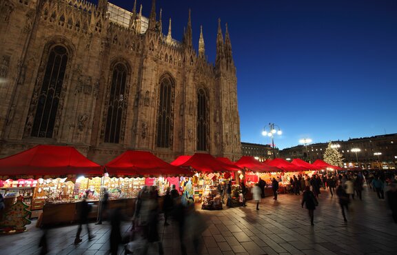 Serie di gazebo rossi di Natale 6x4m con frontalino ondulato, pareti laterali chiuse e a mezza altezza con decorazioni natalizie utilizzati ai mercatini di Natale in Piazza Duomo a Milano di sera - Mastertent