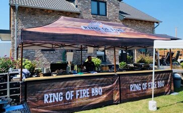 The folding tent of Ring of Fire BBQ stands in the green in front of a house. The folding tent is fully printed.