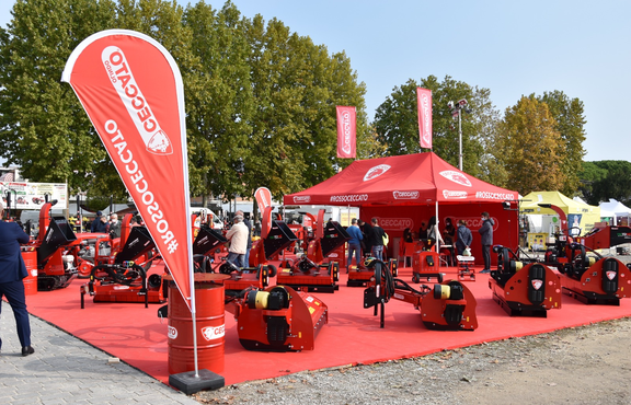 The red gazebo by Ceccato stands in the middle of red machines. Underneath is a red carpet. The exhibition and fair tent has 2 flags on the roof. Another advertising flag is in the front.