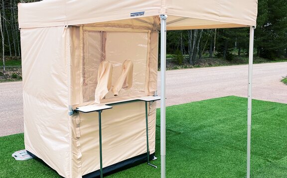 The Covid-19 test cabin in beige has been prepared for the rapid tests. You can see the cabin, the gaiters and the counter in front of it.