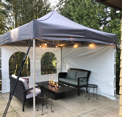 There is a tent with side walls and fairy lights on the terrace. There is a fireplace and garden furniture. 