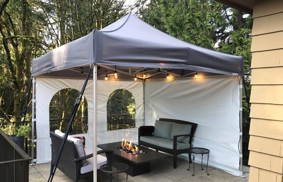 There is a tent with side walls and fairy lights on the terrace. There is a fireplace and garden furniture. 