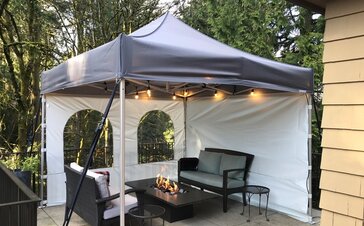There is a tent with side walls and fairy lights on the terrace. There is a fireplace and garden furniture. 