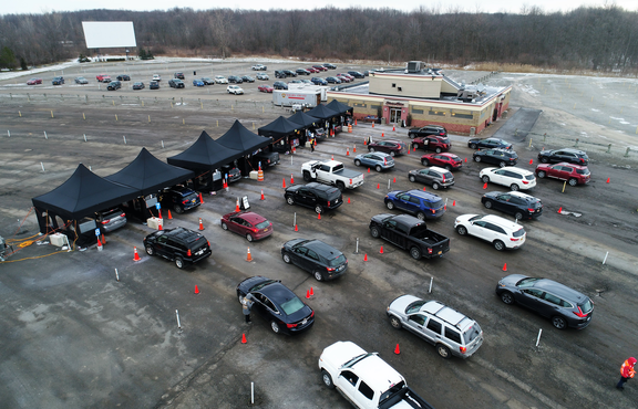 There are 8 black tents in a parking lot in the USA. Cars drive through the testing station next to a building.