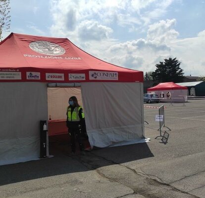 On a parking there are two Rescue tents with white sidewalls and red roofs. Furthermore, there are two green gazebos and an employee in one of the Rescue tents..