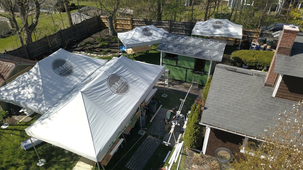 Four folding gazebos of different sizes are standing in a garden next to a house.