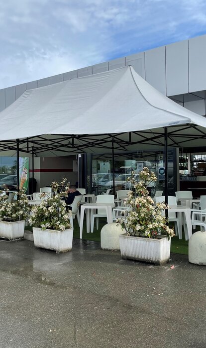 Il gazebo pieghevole grigio chiaro 8x4 m con 4 tettoie serve come copertura della terrazza del bar Mar'n'go in Italia. Tavoli e sedie sono collocati sotto.