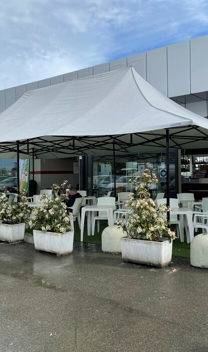 Der hellgraue Faltpavillon 8x4 m mit 4 Vordächern dient als Terrassenüberdachung der Bar Mar'n'go in Italien. Darunter stehen Tische und Stühle.