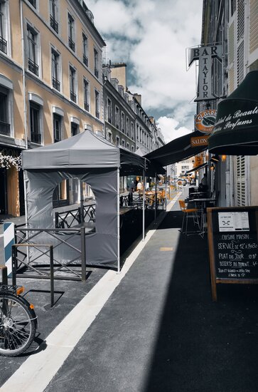 In a street in front of a bar are two black folding gazebos with a sidewall with a round-arched windows.