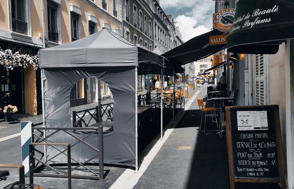 In a street in front of a bar are two black folding gazebos with a sidewall with a round-arched windows.