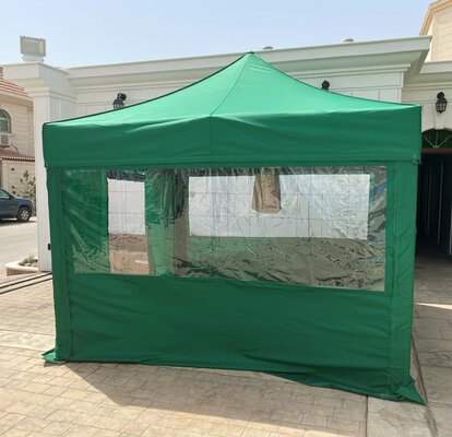 A green folding gazebo is standing on a terrace. It has four sidewalls, a rolled-up door at the front and a large panorama window on the left and right side.