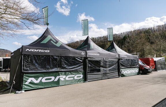 Three black folding gazebos with green logos are standing next to each other. All of them have a flag on the roof.