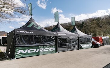 Three black folding gazebos with green logos are standing next to each other. All of them have a flag on the roof.