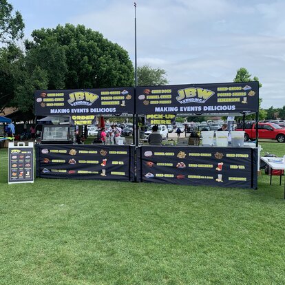 Deux tents pliants noirs imprimés sont placés côte à côte sur une pelouse. Ce sont des stands où l'on vend des boissons et de la nourriture.