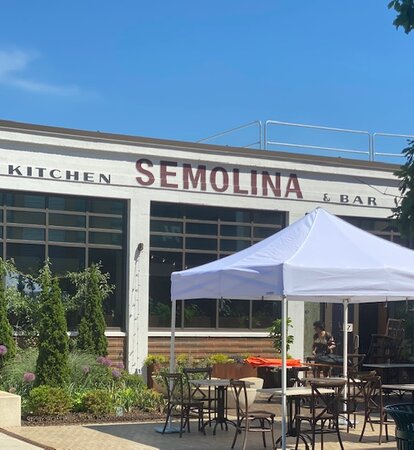 Auf der Terrasse eines Restaurants steht ein weißer Faltpavillon. Darunter befinden sich Tische und Stühle.