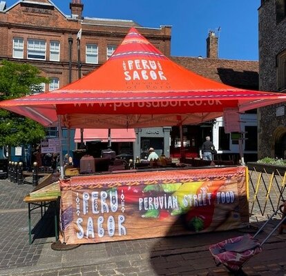 Su una piazza c'è un gazebo pagoda rosso con banco. Ha pareti laterali a metà altezza che sono, come anche il tetto, stampati sulla superficie intera. È uno stand street food.