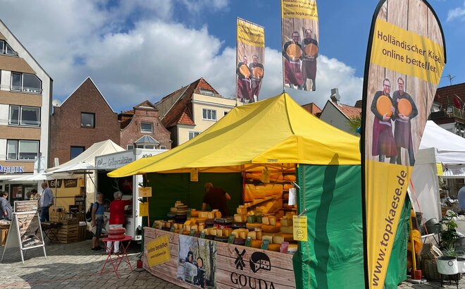 The 4.5x3 m yellow market gazebo has a green canopy and side walls. Customised flags to increase visibility and half a wall fully sublimation-printed