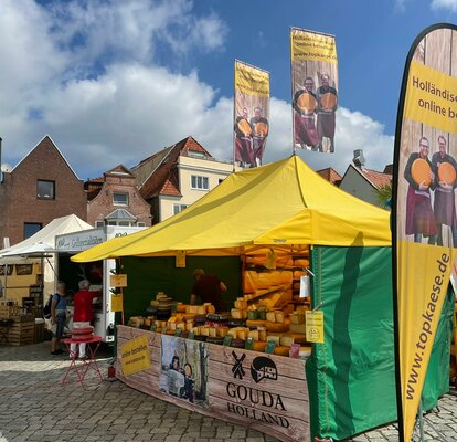 The 4.5x3 m yellow market gazebo has a green canopy and side walls. Customised flags to increase visibility and half a wall fully sublimation-printed