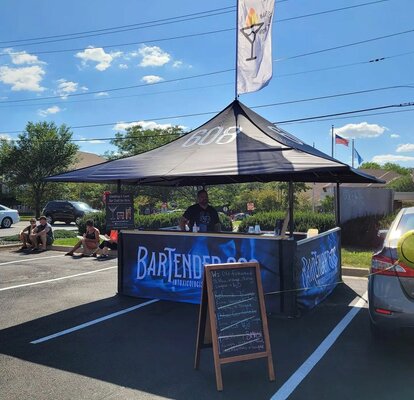 On the picture there is a black, printed folding gazebo with wooden counter and a roof-flag, It is a cocktail bar.