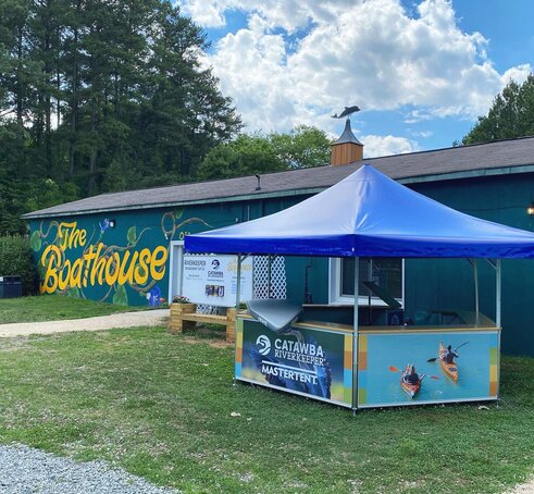 A Mastertent pavilion set up as a check-in station for kayak rentals. Designed with a blue roof and printed photos around the base panels.