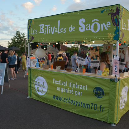 C'è un gazebo pieghevole verde con tetto piatto e un bancone di legno. Il gazebo è illuminato e sullo sfondo si vedono alcune persone.