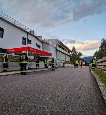 Next to a road there is a red and white fire brigade tent. Several firemen can be seen around the tent.