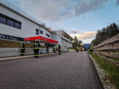 Accanto a una strada c'è un gazebo pieghevole per vigili del fuoco rosso e bianco. Intorno al gazebo ci sono diversi pompieri.