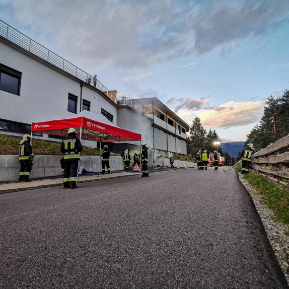 Accanto a una strada c'è un gazebo pieghevole per vigili del fuoco rosso e bianco. Intorno al gazebo ci sono diversi pompieri.