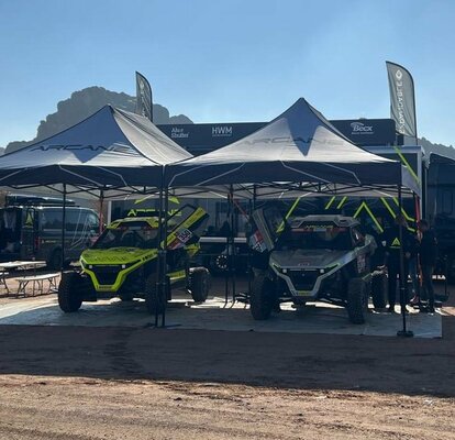 two black and white race gazebos at Dakar rally 2022 with black Arcane van and cars near the mountains in the sand