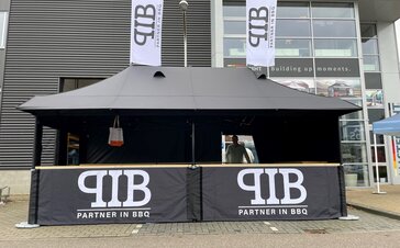 Schwarzes Raucherzelt mit Logo und weißen Fahnen mit Vordach und Streetfood-Theke von Partner in BBQ in den Niederlanden