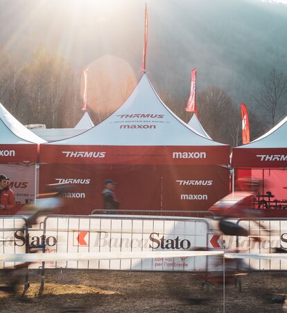 Auf dem Bild sind drei Faltpavillons mit roter Dachflagge des Mountainbike-Teams Thömus Maxon zu sehen. Sie haben weiße Dächer und rote Seitenwände. Im Hintergrund sieht man noch drei weitere Dachspitzen mit den Flaggen.