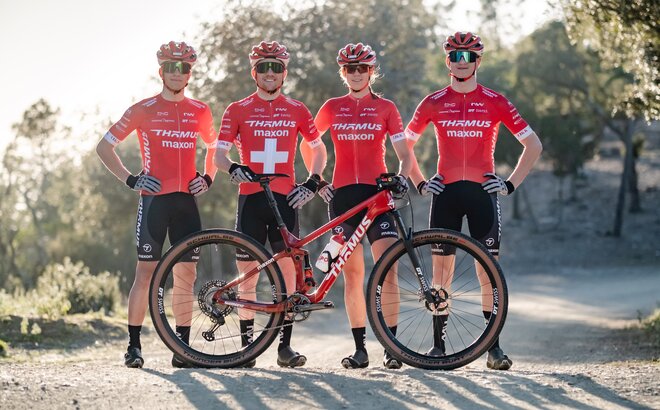 Four mountain bike racers of the Swiss team stand next to each other, a bicycle in front of them.
