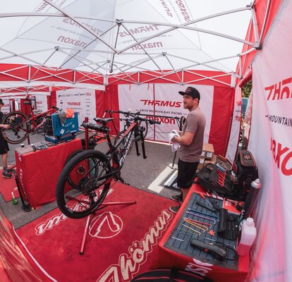 Under a folding gazebo, two men who are repairing mountain bikes can be seen.