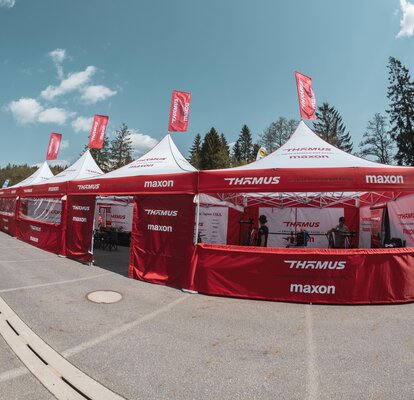 Four red and white folding gazebos are standing next to each other on a square. They have red roof flags.