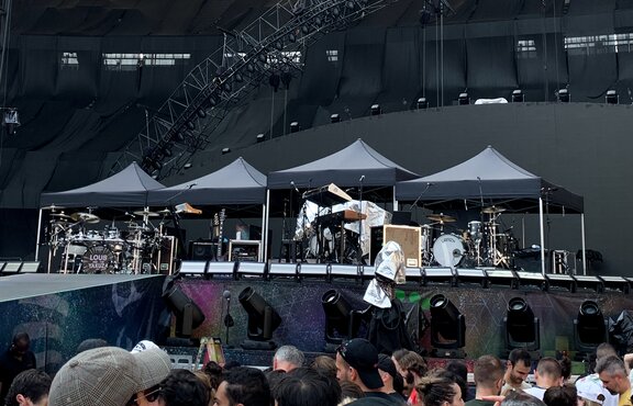 There are four black 3x3 m folding gazebos on a stage and Coldplay's instruments underneath them.