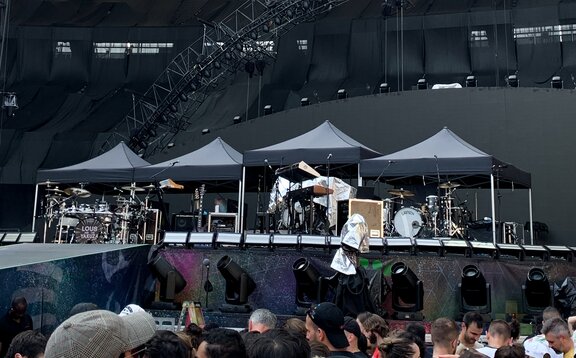 There are four black 3x3 m folding gazebos on a stage and Coldplay's instruments underneath them.