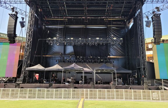 On a stage, before a Sting concert, there are seven 3x3 m black folding gazebos that serve as protection for the technical equipment.