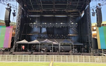 Auf einer Bühne vor einem Sting-Konzert stehen sieben 3x3 m große schwarze Faltzelte, die als Schutz für die technische Ausrüstung dienen.