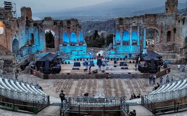 Nel Teatro Antico di Taormina ci sono due gazebo pieghevoli neri di 3x3 m a destra e a sinistra del palco. Sotto ci sono i dispositivi tecnici per l'imminente concerto.