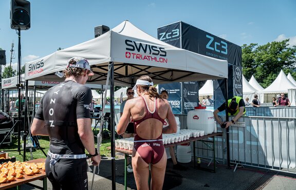 L'immagine mostra due gazebo pieghevoli 3x3 personalizzati. Sotto di essi si trovano bevande per gli atleti.