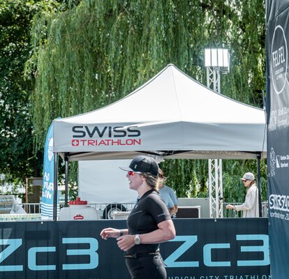 The picture shows a female runner and in the background a grey 3x3 m folding gazebo with a logo on the roof.