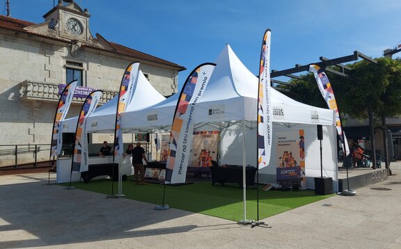 Due gazebo con tetto a pagoda di 5x5 m si trovano uno accanto all'altro su una piazza. Intorno ai gazebo promozionali ci sono anche sei bandiere stampate e personalizzate.