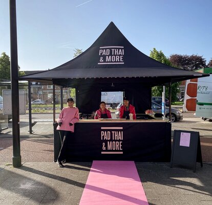 The picture shows a black 3x3 m folding gazebo, printed with the Pad Thai logo. The folding gazebo has a sidewall with a door and a half-height sidewall with a counter where the food is served.