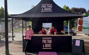 A black 10x10 4-awning canopy tent with counters set up for cooking and vending Thai food.