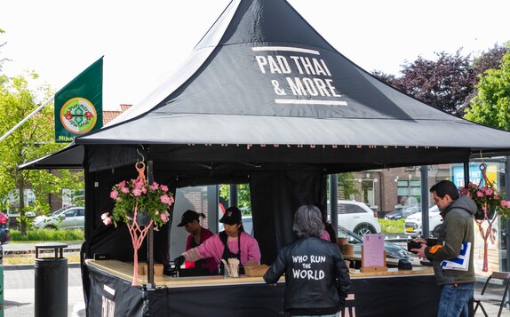 The picture shows a black 3x3 m folding gazebo, printed with the Pad Thai logo. The folding gazebo has a sidewall with a door and a half-height sidewall with a counter where the food is served.
