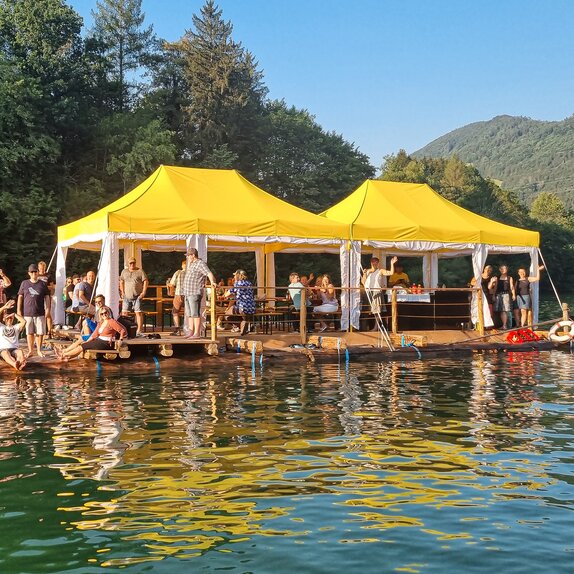 Raft trip on mountain river with tourist group and 2 Mastertent folding pavilions in yellow and white custom-made for weather protection on raft with mountains in the background