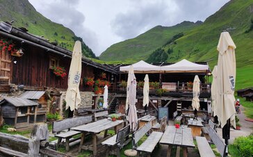 Zwei beige Faltpavillons mit Pirontex-Stoff steht auf einer Terrasse einer Hütte, daneben stehen Tische und Bänke.