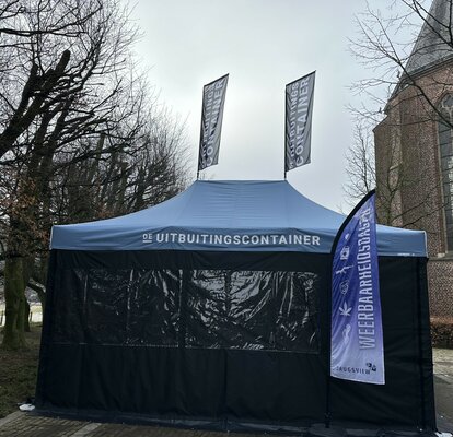 You can see a blue 6x4 m folding gazebo. It has two large windows at the front. There are also two flags on the roof and one in front of the tent. A white logo can be seen on the roof and the flags.