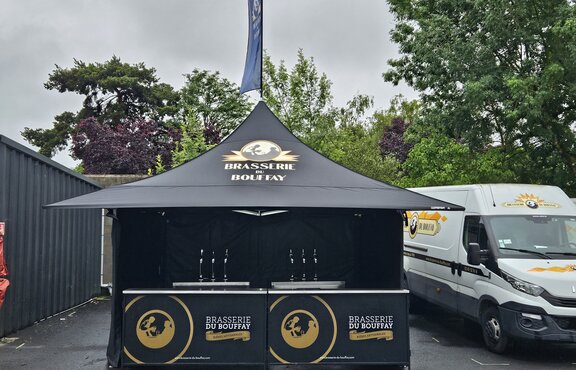 The picture shows a black 3x3 m folding gazebo with a personalised print on the sidewalls, roof and roof flag. The gazebo also has four awnings.